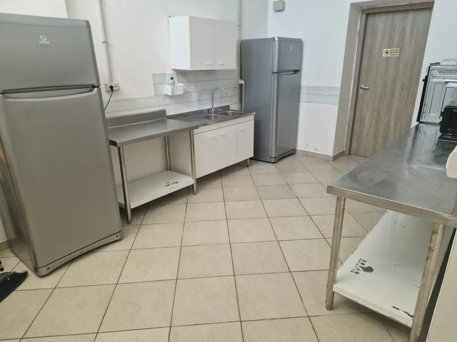Zona cucina con frigoriferi, lavello e piani in acciaio